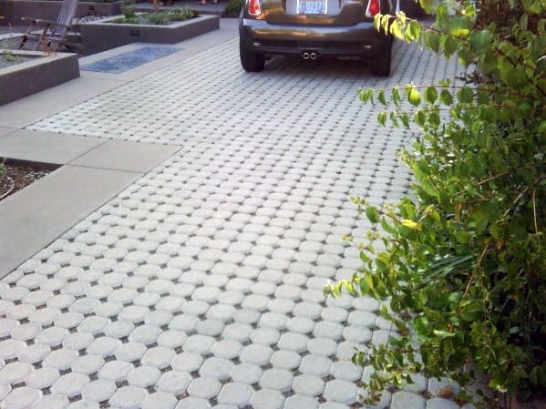 Permeable hexagonal paver driveway with smooth concrete edging near landscaped greenery.