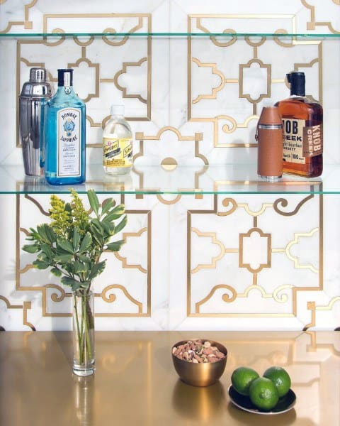 Elegant mini bar with glass shelves, gold-patterned backsplash, and a luxurious golden countertop featuring a vase and small bowls.