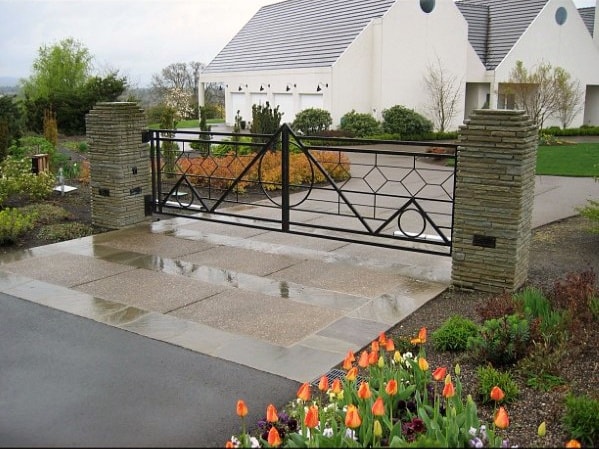 Black metal driveway gate with geometric patterns, set between stone pillars.