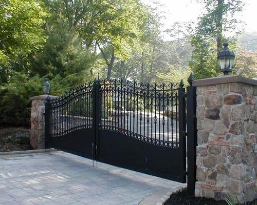 Decorative black iron driveway gate with arched top and spiked finials.