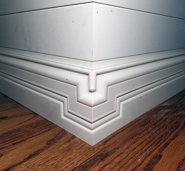 Ornate white baseboard with intricate detailing and polished wood flooring.