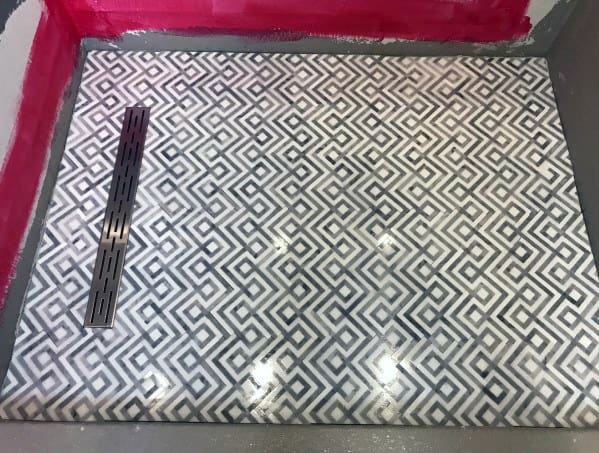Shower floor boasts black and white geometric tiles with a sleek linear drain