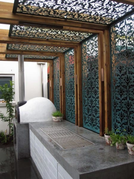 Pergola with intricate metal panels, concrete countertop, and built-in outdoor grill station.