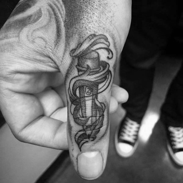 A black and white tattoo of a dagger elegantly inked on a finger, with intricate decorative ribbons reminiscent of pencil sketches