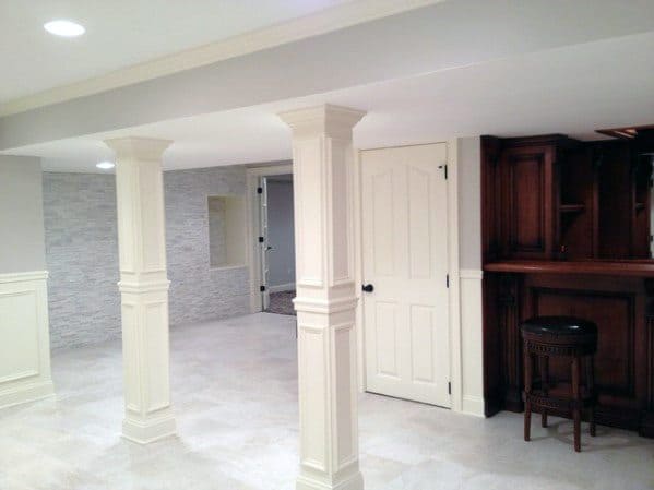 Basement with ornate white millwork poles, tile flooring, and built-in wooden bar.