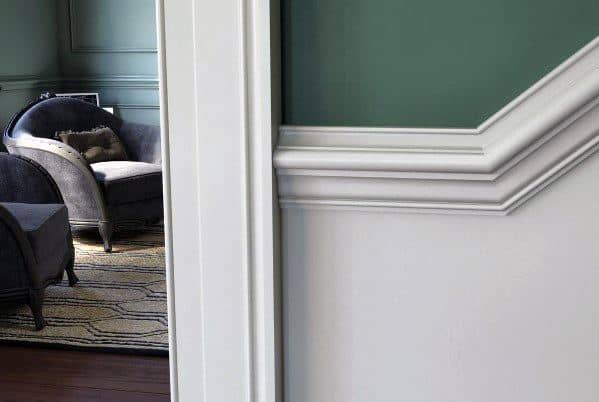 Close-up of an interior wall with decorative molding and a chair rail, blurred seating area with chairs in the background