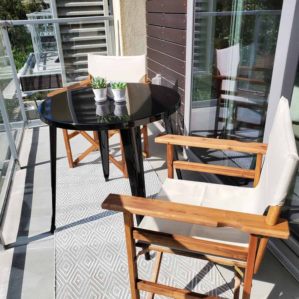 Small balcony with wooden chairs, black round table, and decorative succulents.