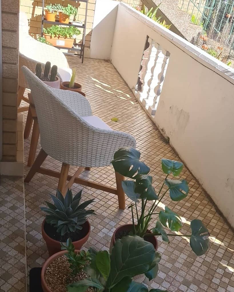 Balcony with white wicker chairs, potted plants, and small garden shelf in a sunny space.