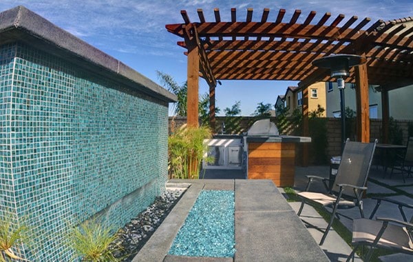 Modern outdoor wall fountain with blue mosaic tiles, pergola, and seating area,