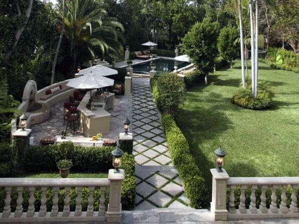 Mediterranean-style patio bar with stone countertops, umbrella seating, and lush garden surroundings.