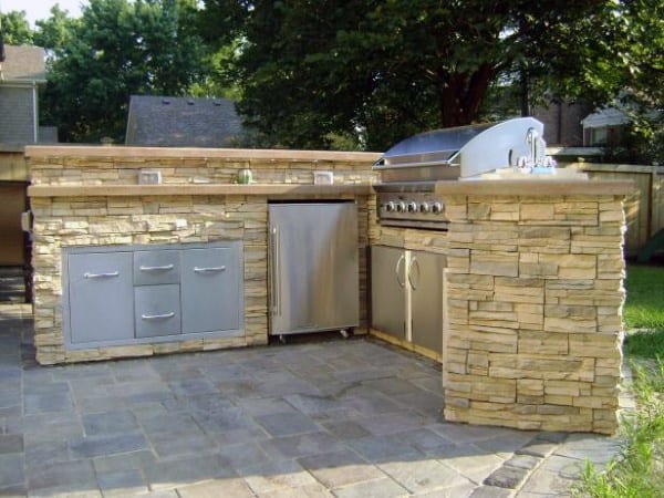 Outdoor stone kitchen with stainless steel cabinets, grill, and refrigerator on a spacious patio