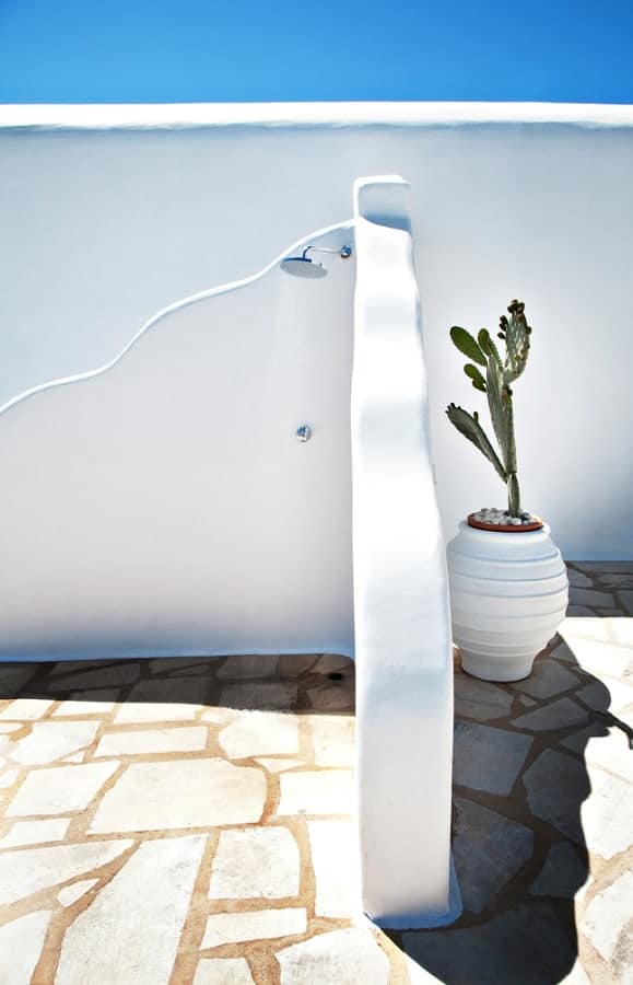 Minimalist outdoor shower with white stucco walls, a potted cactus, and stone tile flooring.