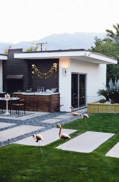 Modern wood pallet bar with string lights, outdoor seating, and decorative flamingos on a landscaped lawn.