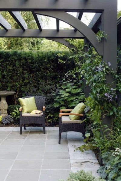 Traditional pergola with arched beams, wicker chairs, lush greenery, and a serene patio setting.