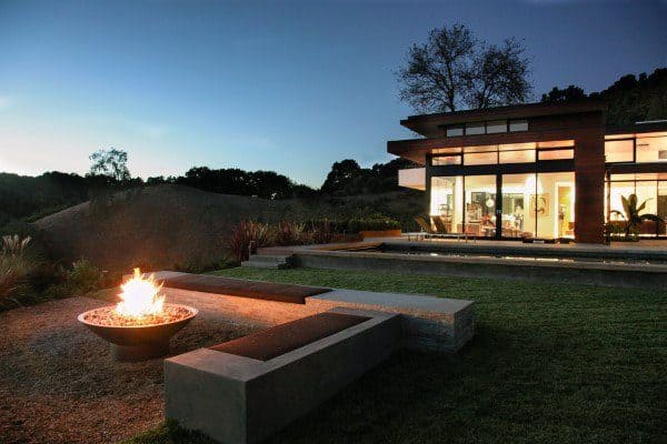Modern house with large windows, a cozy fire pit, and scenic landscape at dusk