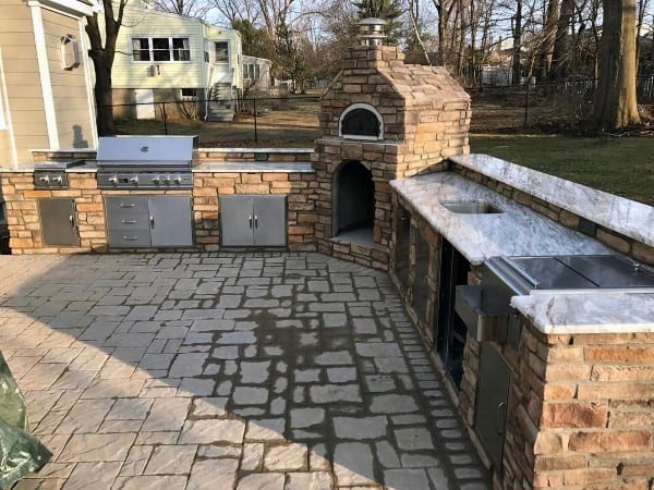 Outdoor kitchen with grill, oven, and countertops set on an outdoor stone patio with a brick and stone facade