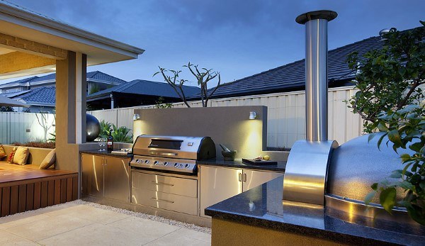 Outdoor kitchen featuring a stainless steel grill and pizza oven, surrounded by patio seating and ambient lighting