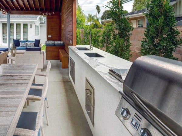 Outdoor kitchen with a marble countertop, outdoor grill, and dining area, surrounded by lush greenery