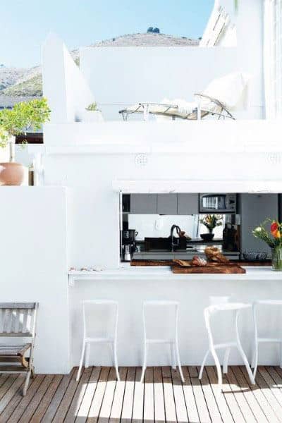 White outdoor bar with a floating counter, minimalist bar stools, and open-air kitchen access.