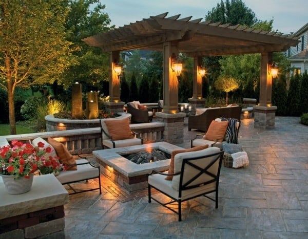 A cozy patio with a pergola, fire pit, cushioned chairs, and ambient lighting at dusk