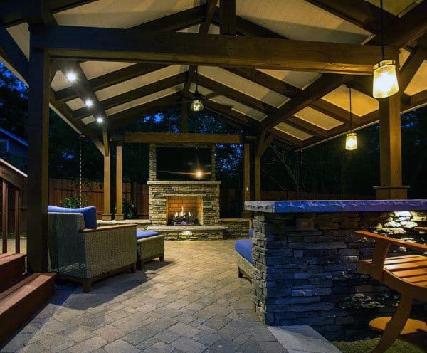 Cozy pavilion with exposed wooden beams, stone fireplace, seating area, and warm lighting for evening relaxation.