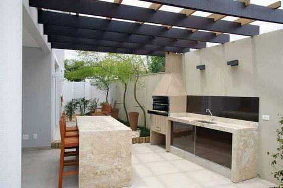 Outdoor bar with stone countertops, built-in barbecue, and wooden pergola for shade.