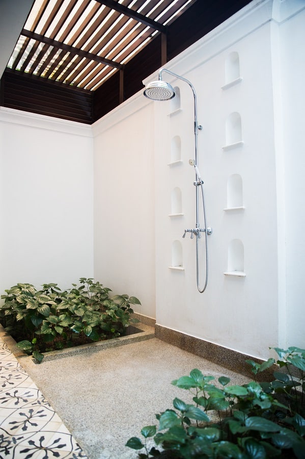 Elegant outdoor shower with a rain showerhead, wall niches, greenery, and a slatted wooden ceiling.