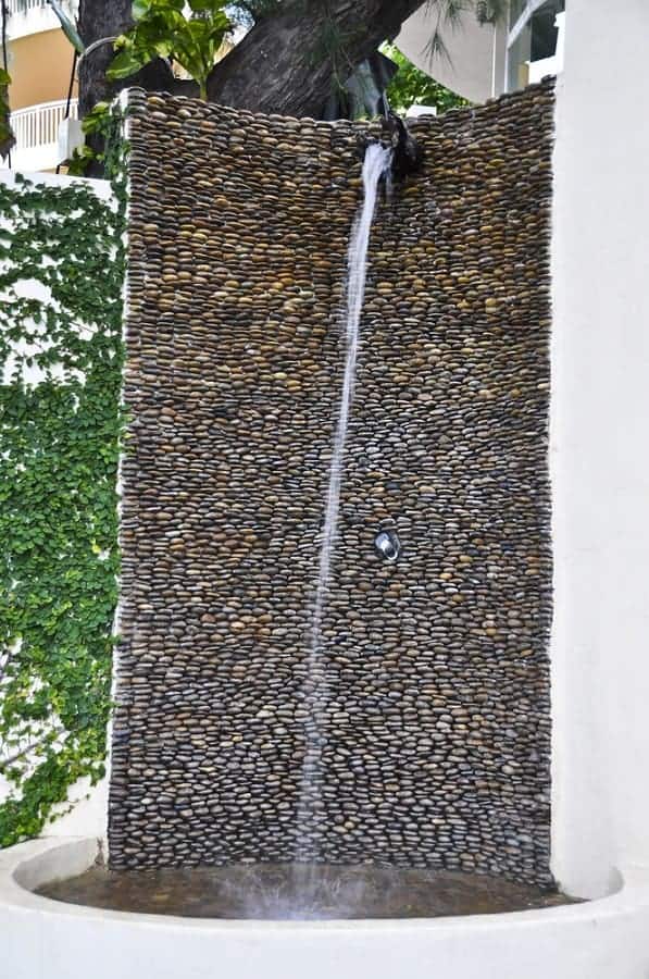 Pebble stone outdoor shower wall with cascading water feature for a natural and relaxing ambiance.