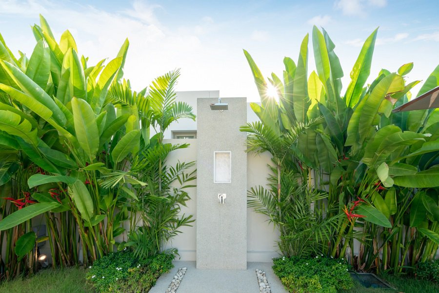Minimalist outdoor shower with a sleek concrete wall, surrounded by vibrant tropical greenery.