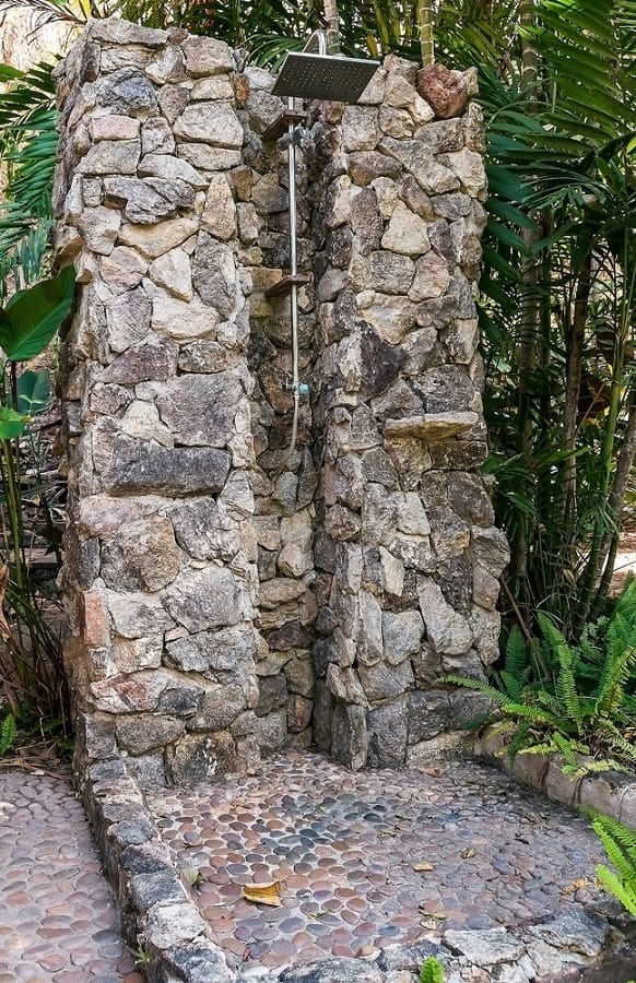 Rustic stone outdoor shower with a natural design, blending seamlessly into a lush garden setting.