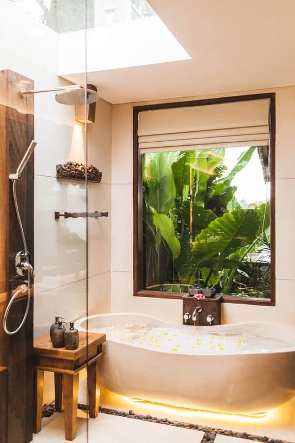 Luxurious outdoor bathroom with a soaking tub, glass shower, and lush greenery view.