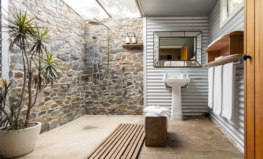 Rustic outdoor shower with stone walls, corrugated metal siding, and natural wood accents.
