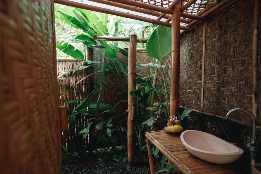 Bamboo outdoor shower featuring natural woven walls, lush greenery, and a rustic stone basin for a tropical retreat.
