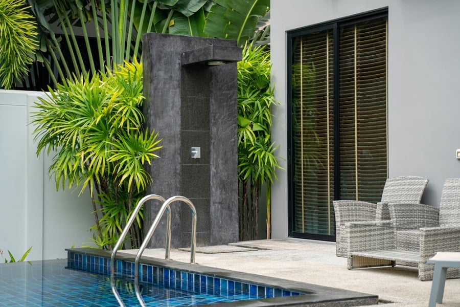 Modern stone outdoor shower by the pool with lush greenery.