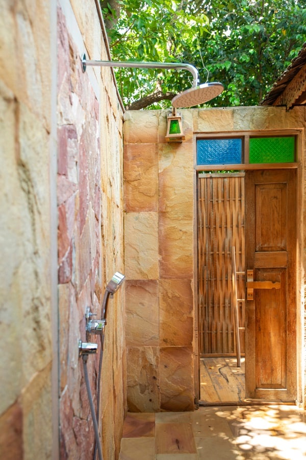 Outdoor shower with natural stone walls, colorful glass panels, and a wooden door.