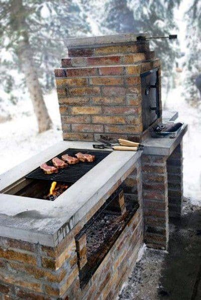 Outdoor brick barbecue grill with steaks sizzling in a snowy forest setting