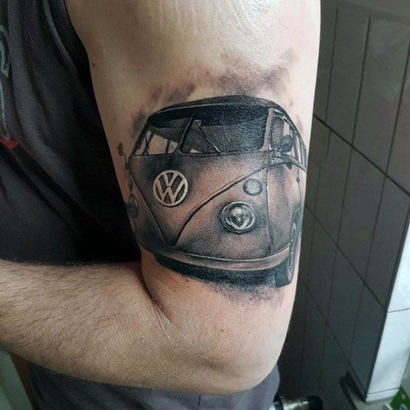 Black and gray tattoo of a classic Volkswagen van on the upper arm, featuring smooth shading and a front-facing perspective.