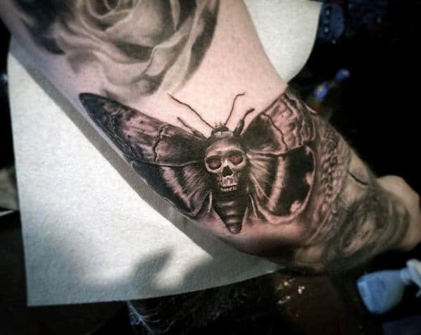 A tattoo of a moth with a skull on its back on an arm