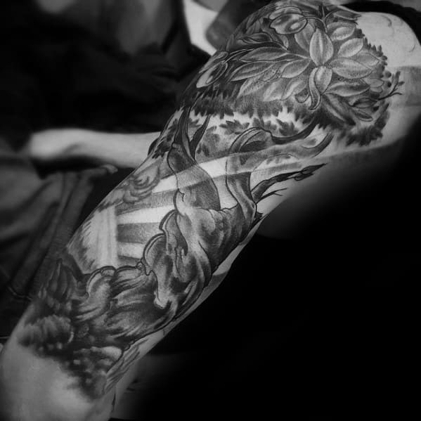 Black and grey realism tattoo of a majestic tree with intricate leaves and a twisting trunk, creating a dynamic and detailed nature-inspired sleeve.