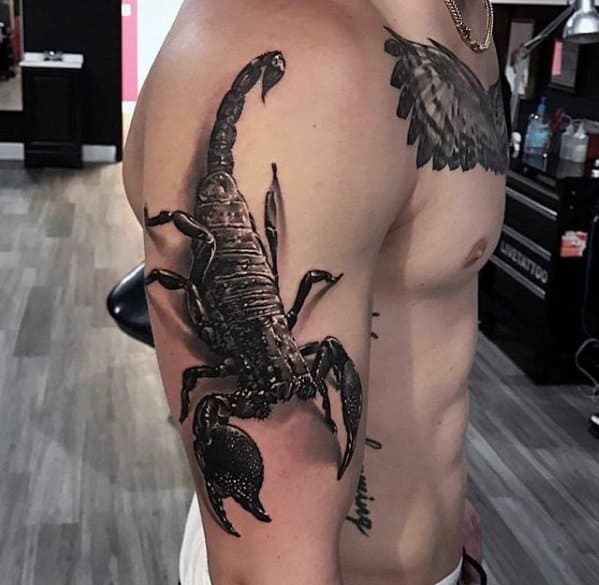 Man with a detailed black scorpion tattoo on his upper arm and shoulder, standing in a tattoo parlor