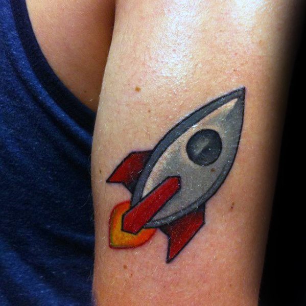 Colorful tattoo of a rocket ship emoji with red fins and a fiery exhaust on a person’s arm