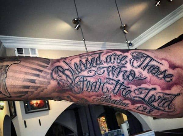 Elaborate cursive script tattoo on the outer bicep reading 'Blessed are those who fear the Lord - Psalm 128,' with shaded background details