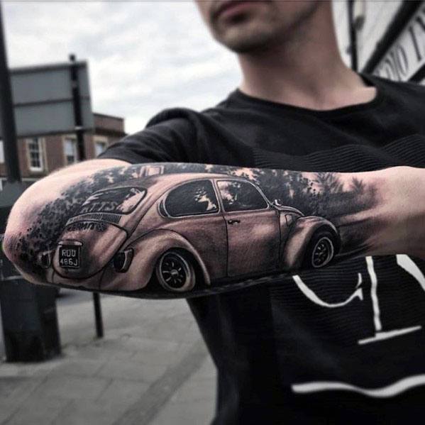 Realistic black and gray tattoo of a classic Volkswagen Beetle on the forearm, shown cruising through a scenic tree-lined road.