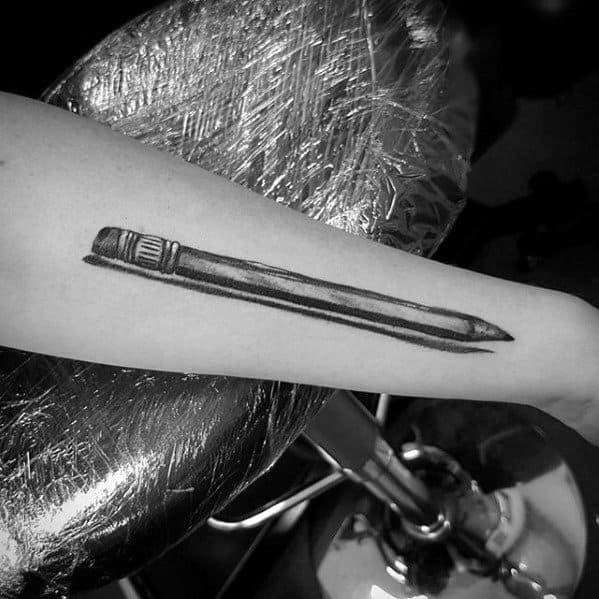 A striking forearm tattoo features a realistic black ink illustration, masterfully capturing the intricate details of a pencil design