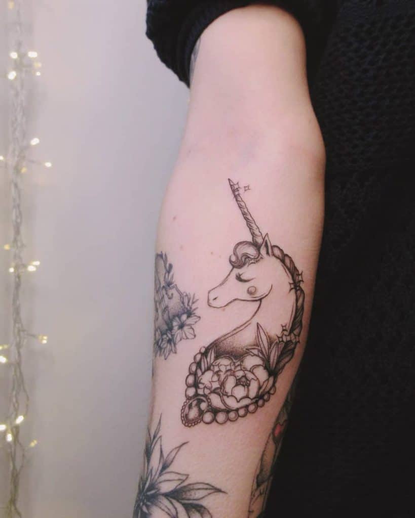 Elegant black ink tattoo of a unicorn with a delicate pearl necklace, surrounded by flowers, creating a mystical and feminine design.