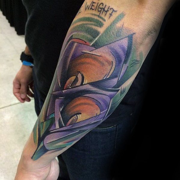 Cubist forearm tattoo featuring intense orange eyes within sharp, layered geometric shapes in shades of purple, green, and blue.