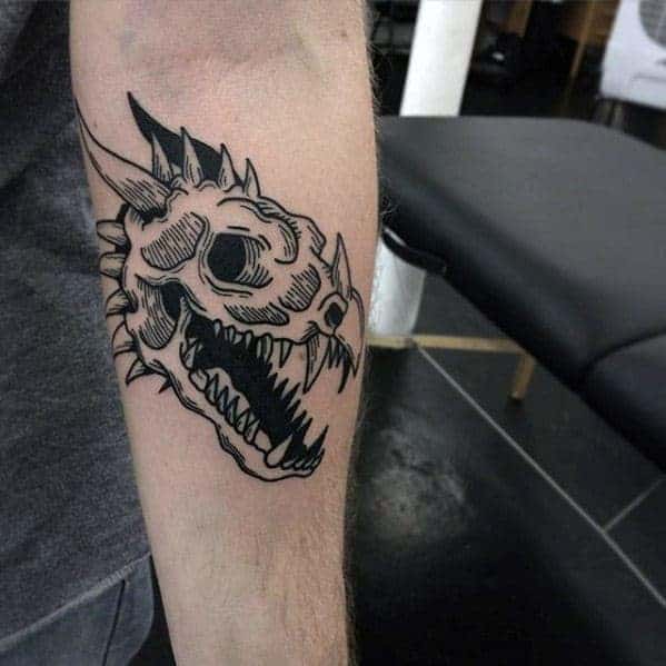 Forearm tattoo featuring a black ink dragon skull