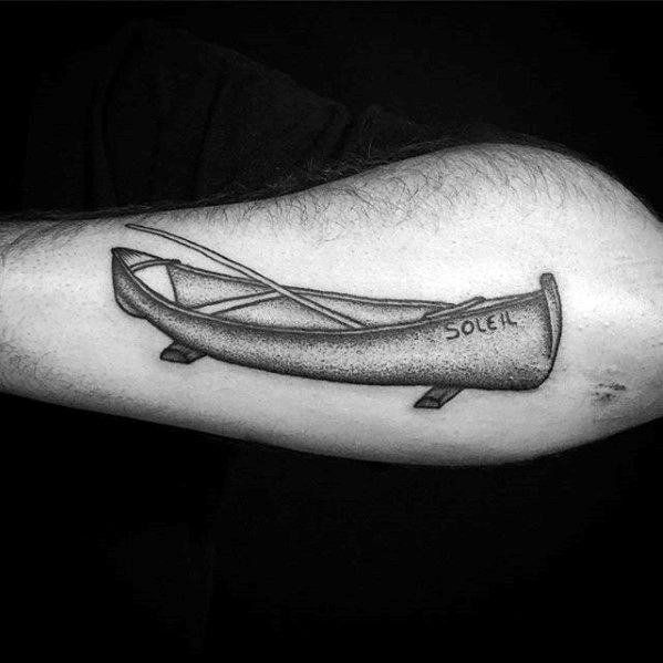 Alt text: Detailed black and grey tattoo of a canoe with paddles, featuring the word "SOLEH" written on the side, done in a realistic style.