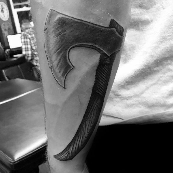 Black and grey hatchet tattoo on the forearm featuring a curved blade, a wrapped grip, and a wood-textured handle, designed with bold shading.