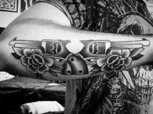Symmetrical tattoo of two revolvers facing outward with roses and a bull skull in the center, blending western and floral themes.